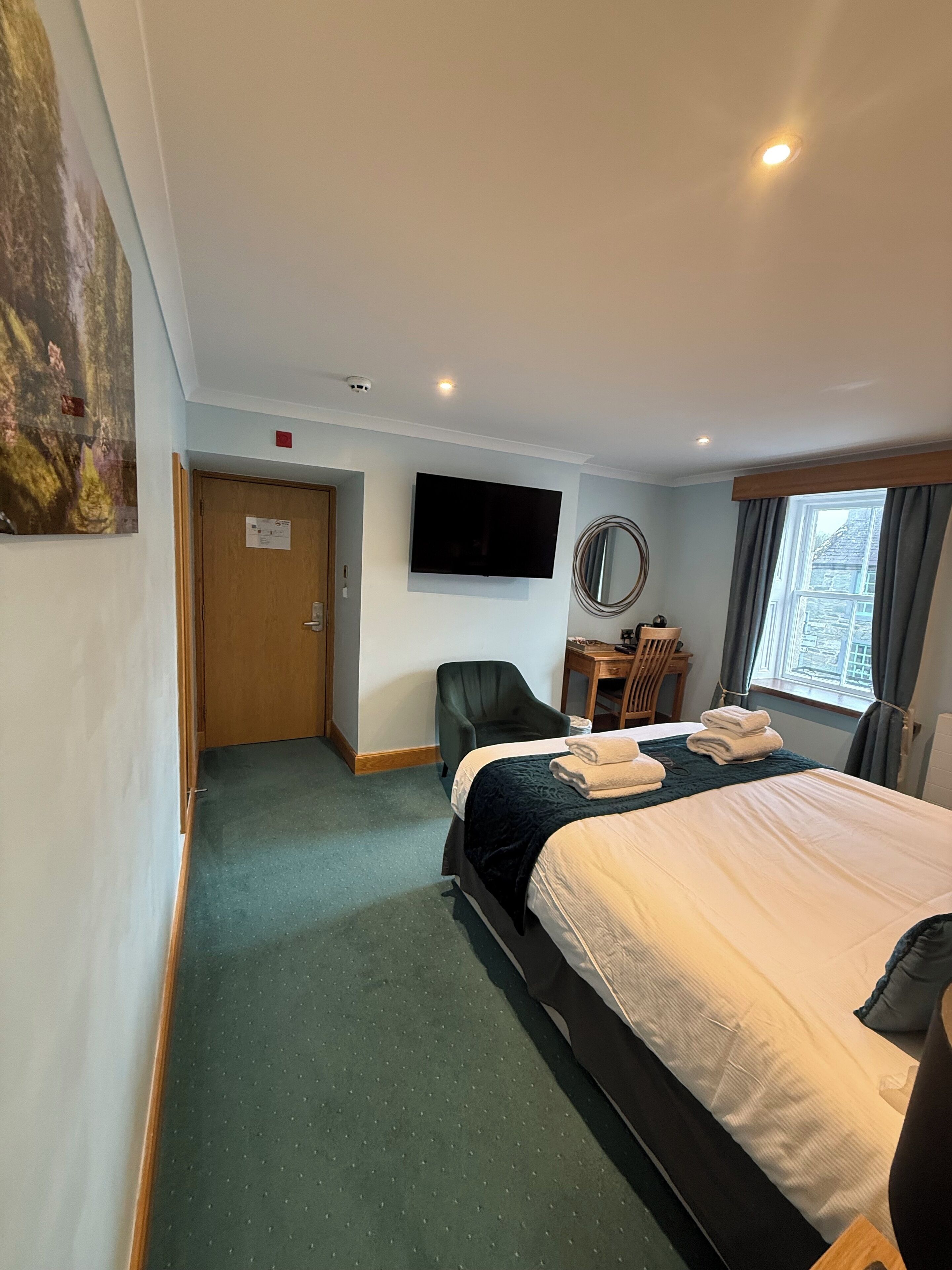 A hotel room with a bed, a desk, a chair, a TV, and a window.