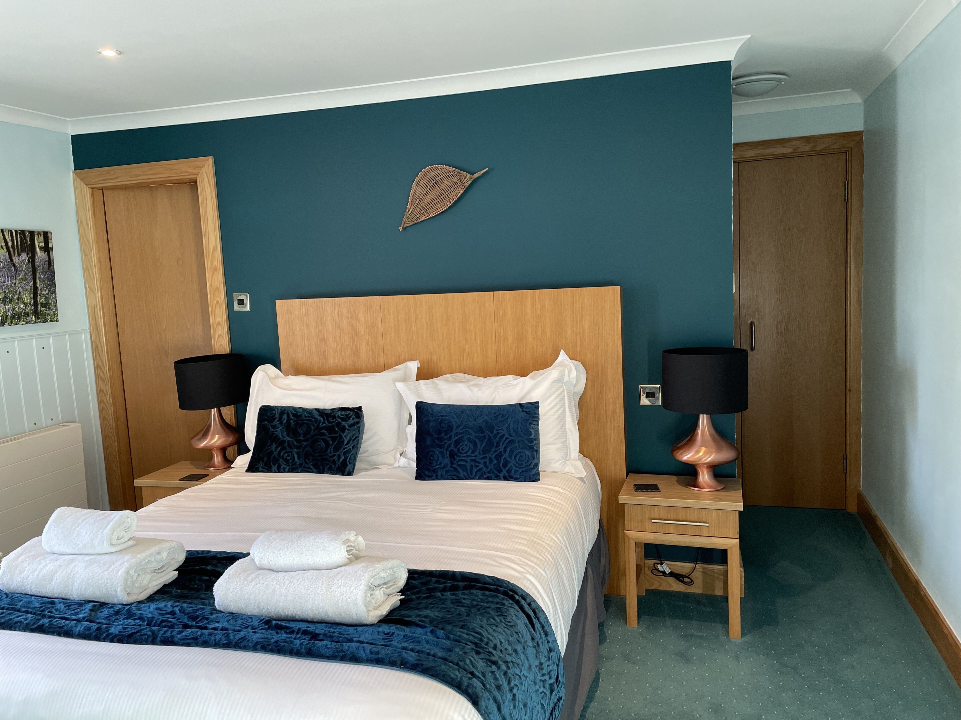 A neatly made bed with white and blue linens, two bedside tables with lamps, and a wooden headboard.