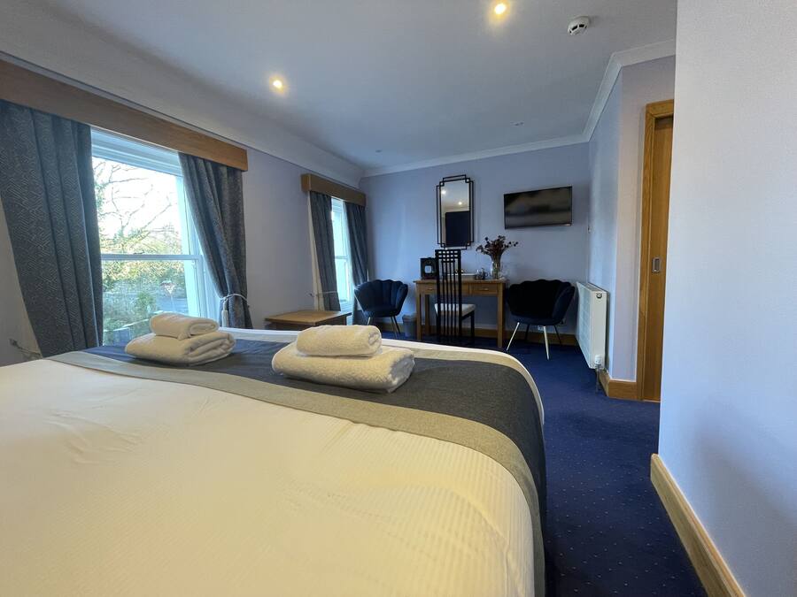 A hotel room with a large bed, two chairs, a desk, a mirror, and a TV.