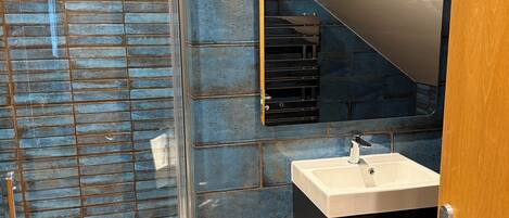 A modern bathroom with a glass shower enclosure, a white sink, and a black cabinet.