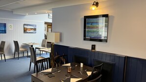A dining area with a table set for four, chairs, a wall-mounted light, and a framed painting. - The Ship Inn (Castle Douglas)