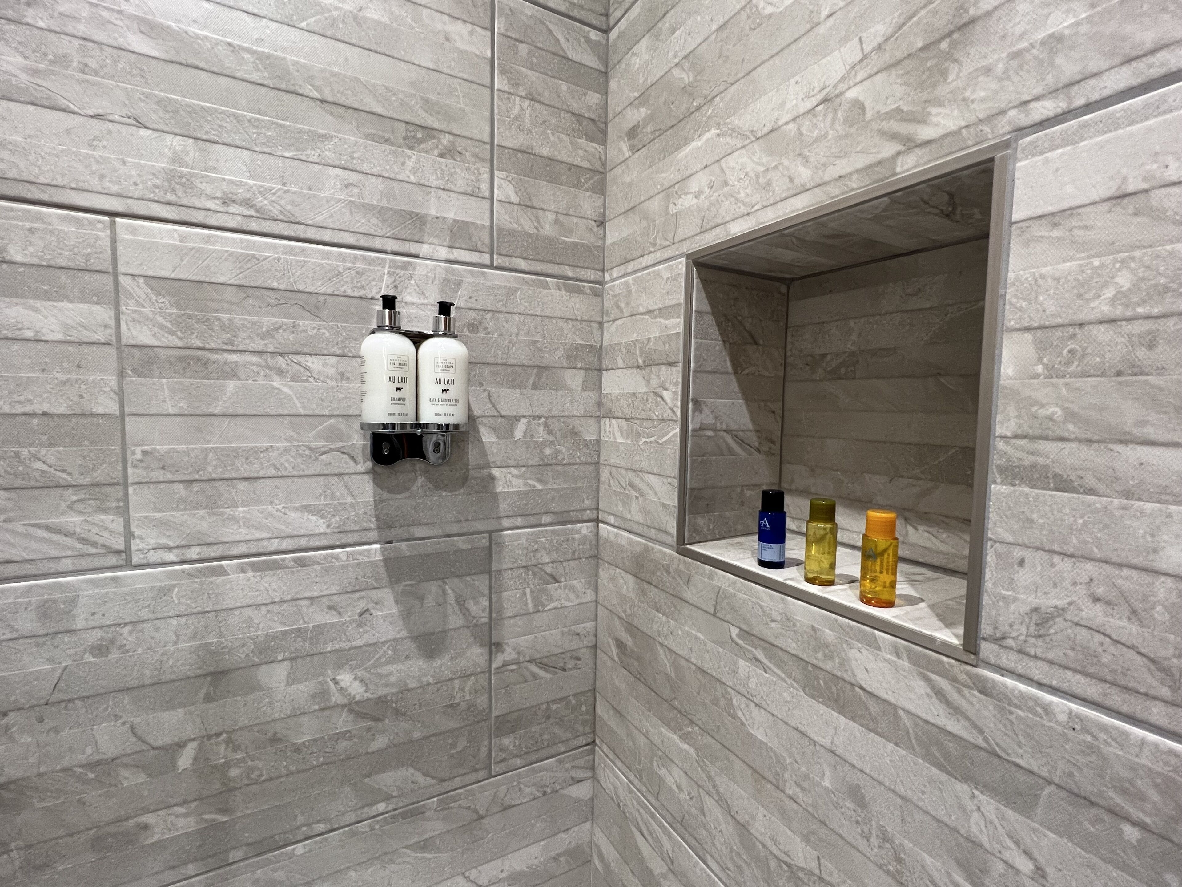 A bathroom with a marble wall, a shelf with toiletries, and a mirror.