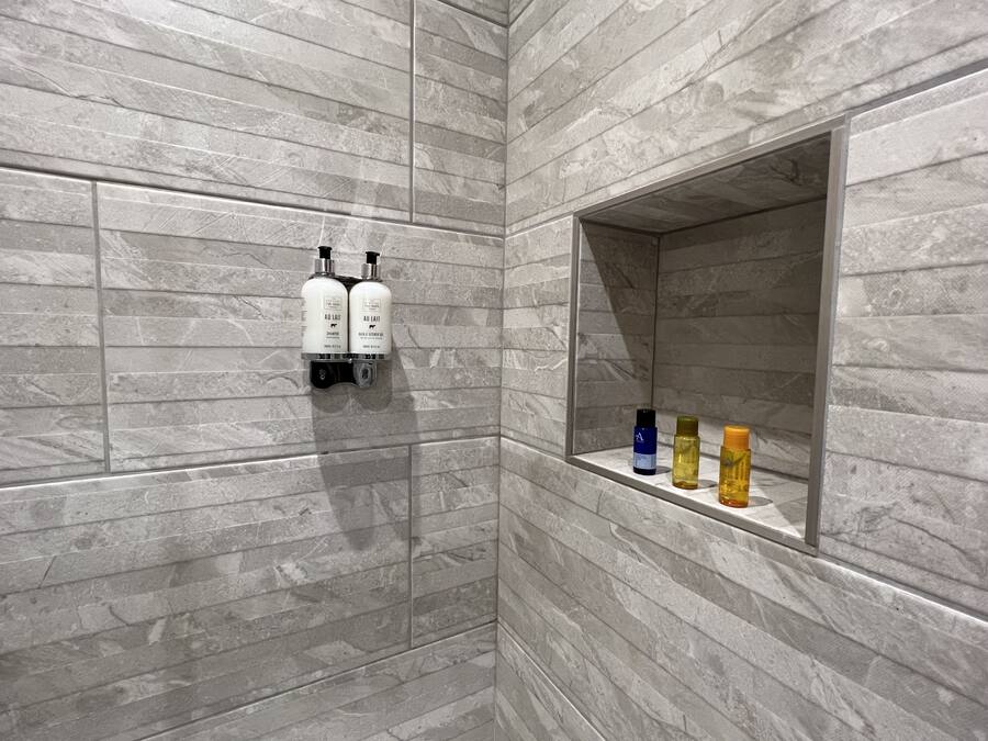 A bathroom with a marble wall, a shelf with toiletries, and a mirror.