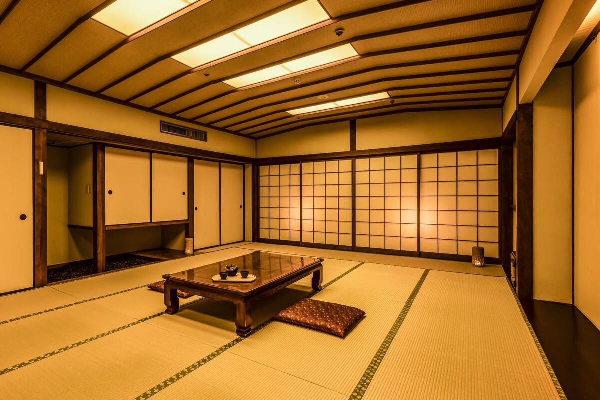 Ein traditioneller japanischer Raum mit Tatami-Boden, Schiebetüren, einem niedrigen Tisch mit Kissen und einem Shoji-Bildschirm.
