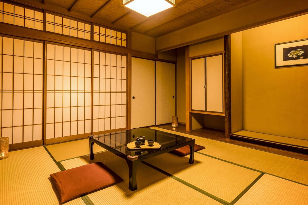 Ein traditioneller japanischer Raum mit Tatami-Böden, einem niedrigen Tisch mit Teeservice, Schiebetüren und einem gerahmten Bild an der Wand.