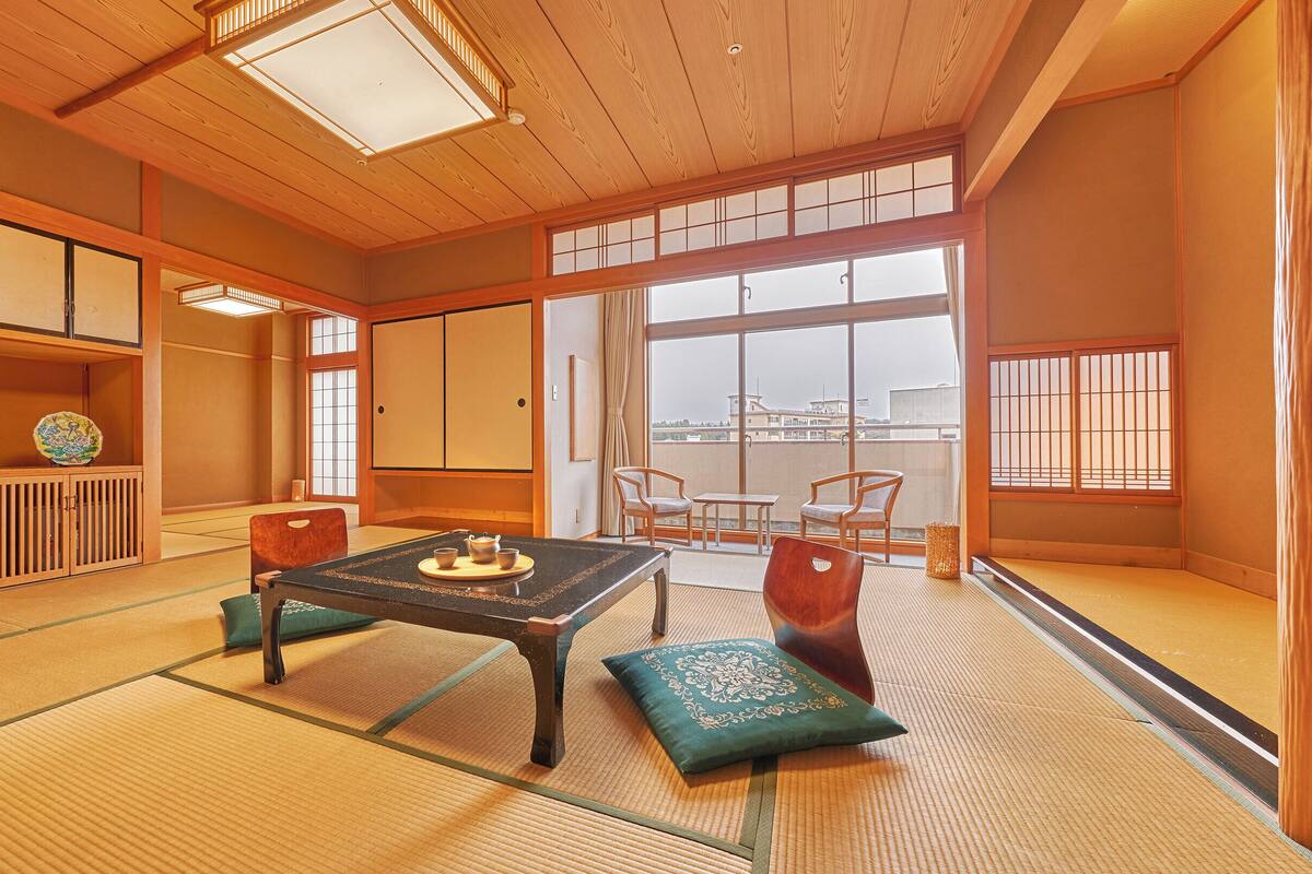Ein traditioneller japanischer Raum mit Tatami-Böden, einem niedrigen Tisch mit Teeservice, Schiebetüren und Blick auf die Stadtlandschaft.