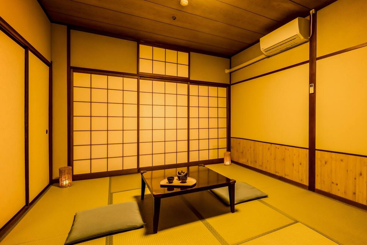 Ein traditioneller japanischer Raum mit Tatami-Boden, einem niedrigen Tisch mit Kissen und verschiebbaren Türen.