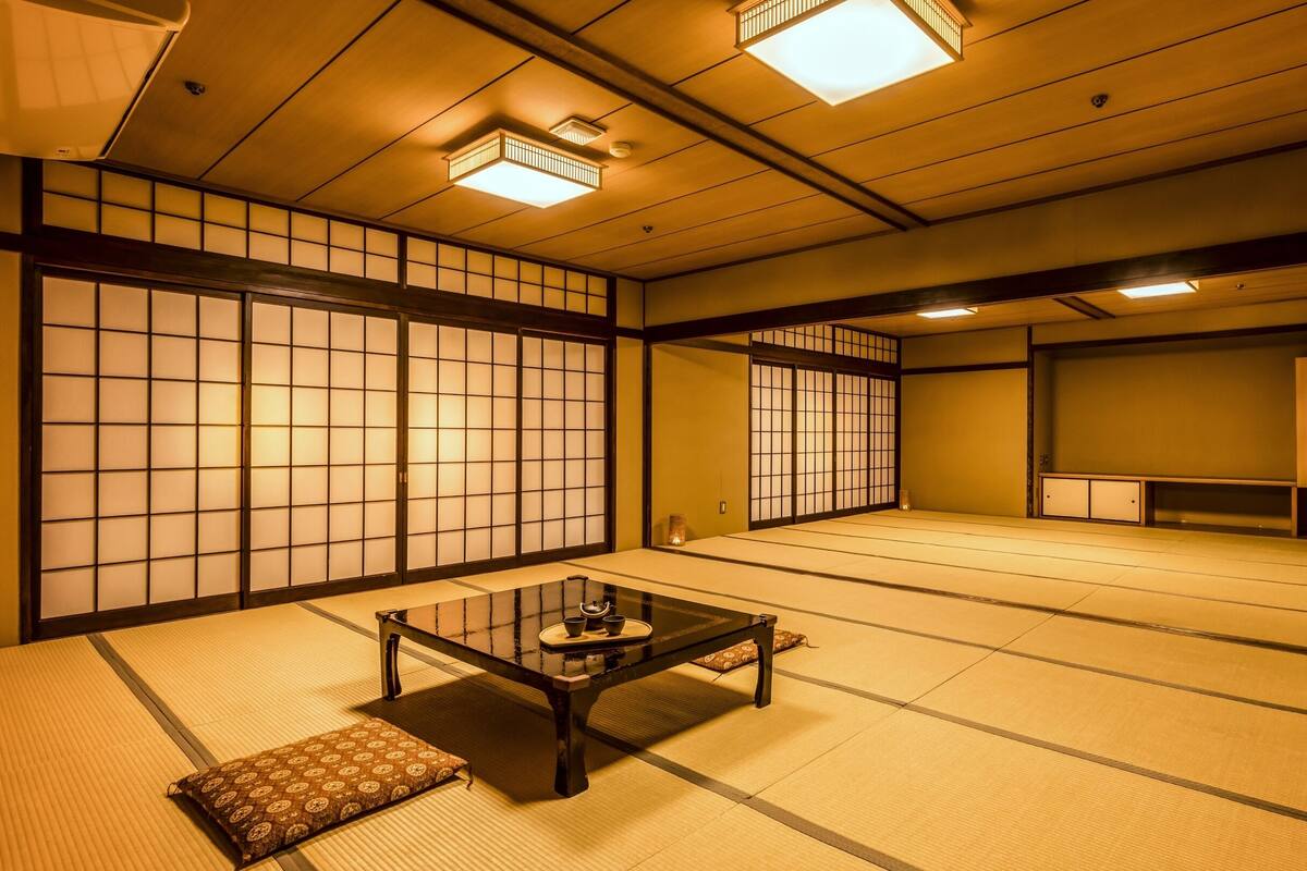 Ein traditioneller Raum mit Tatami-Matten, einem niedrigen Tisch, Kissen, Holztüren, die sich verschieben, und eingelassener Beleuchtung.