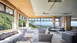 Un área de descanso moderna con sofás y mesas, amplias ventanas que ofrecen vistas a la ciudad y al verdor.