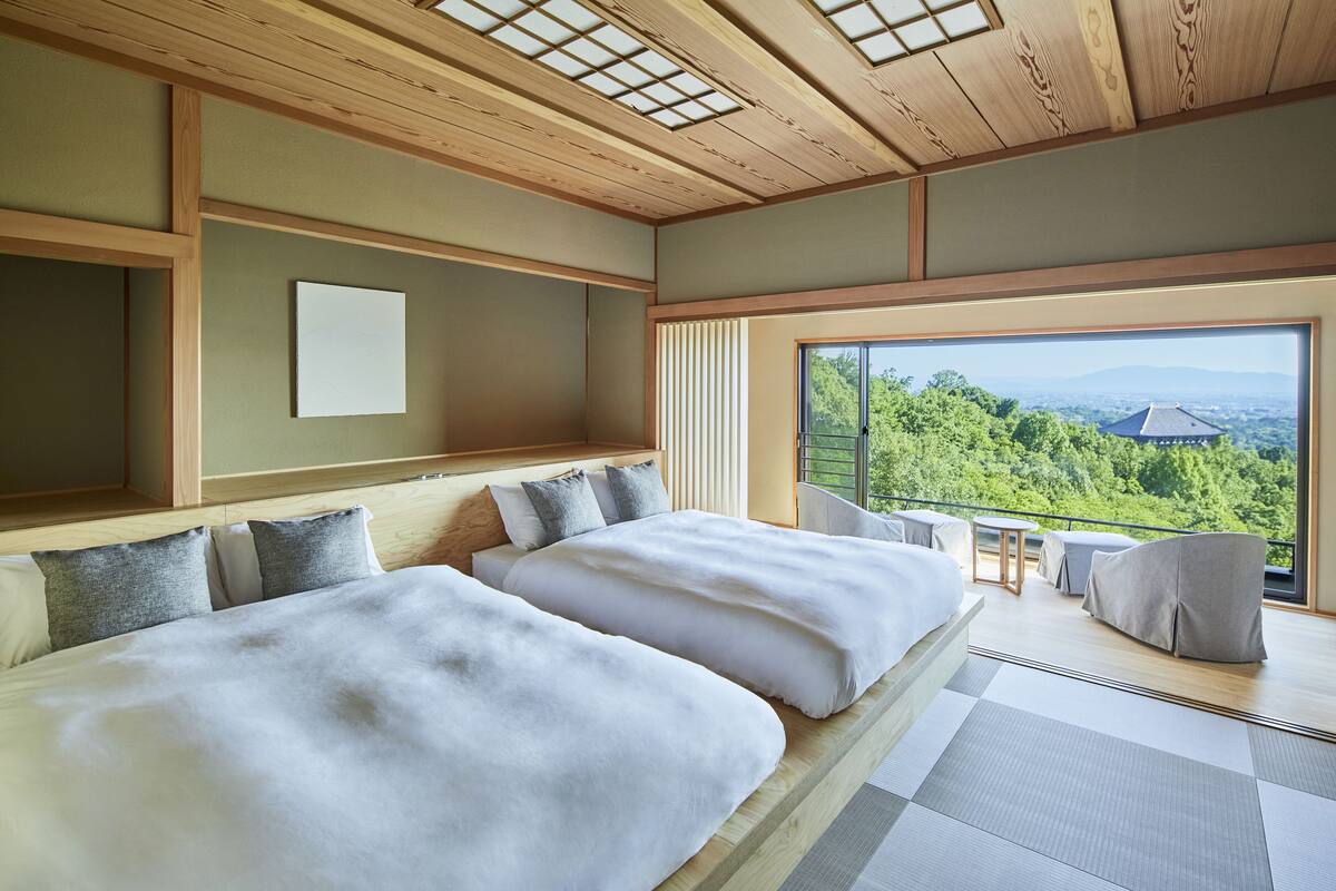 A modern bedroom with two beds, a large window with a view of greenery, and a wooden ceiling.
