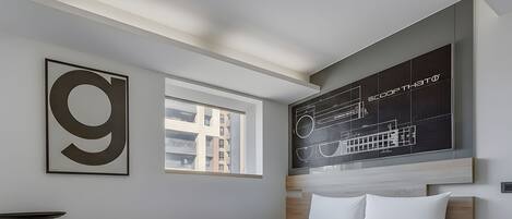 Une chambre d’hôtel moderne dotée d’un grand lit, d’une fenêtre donnant sur la ville et d’un mur orné de plans architecturaux.