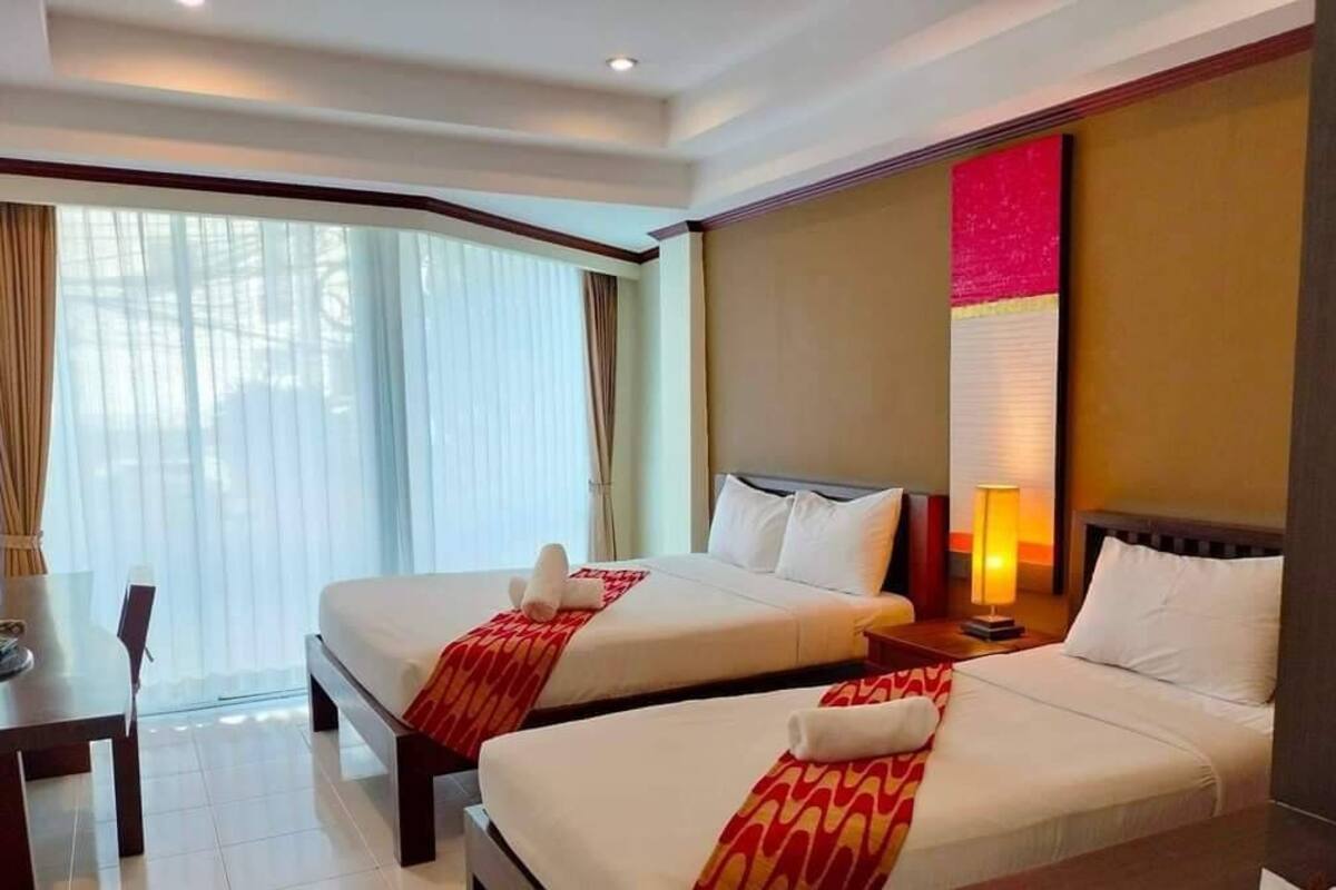 A hotel room with two beds, a desk, and a large window with curtains.