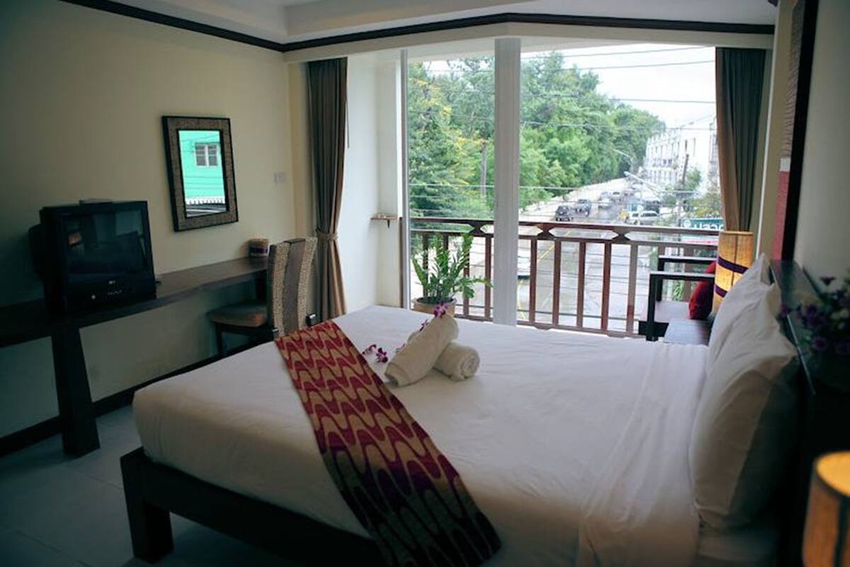 A hotel room with a bed, a television, a balcony with a view of the city, and a window with curtains.