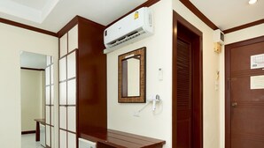 A hotel room with a wooden bench, a wall-mounted air conditioner, a mirror, and a door with a notice. - Khon Kaen Orchid Hotel (Khon Kaen)