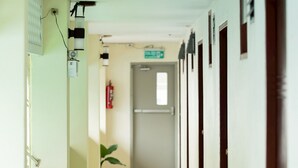 A long, narrow hallway with potted plants on one side, doors on the other, and a fire extinguisher mounted on the wall. - Khon Kaen Orchid Hotel (Khon Kaen)