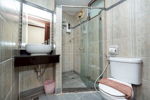 A bathroom with a glass shower enclosure, a white toilet, and a sink with a black countertop. - Khon Kaen Orchid Hotel (Khon Kaen)