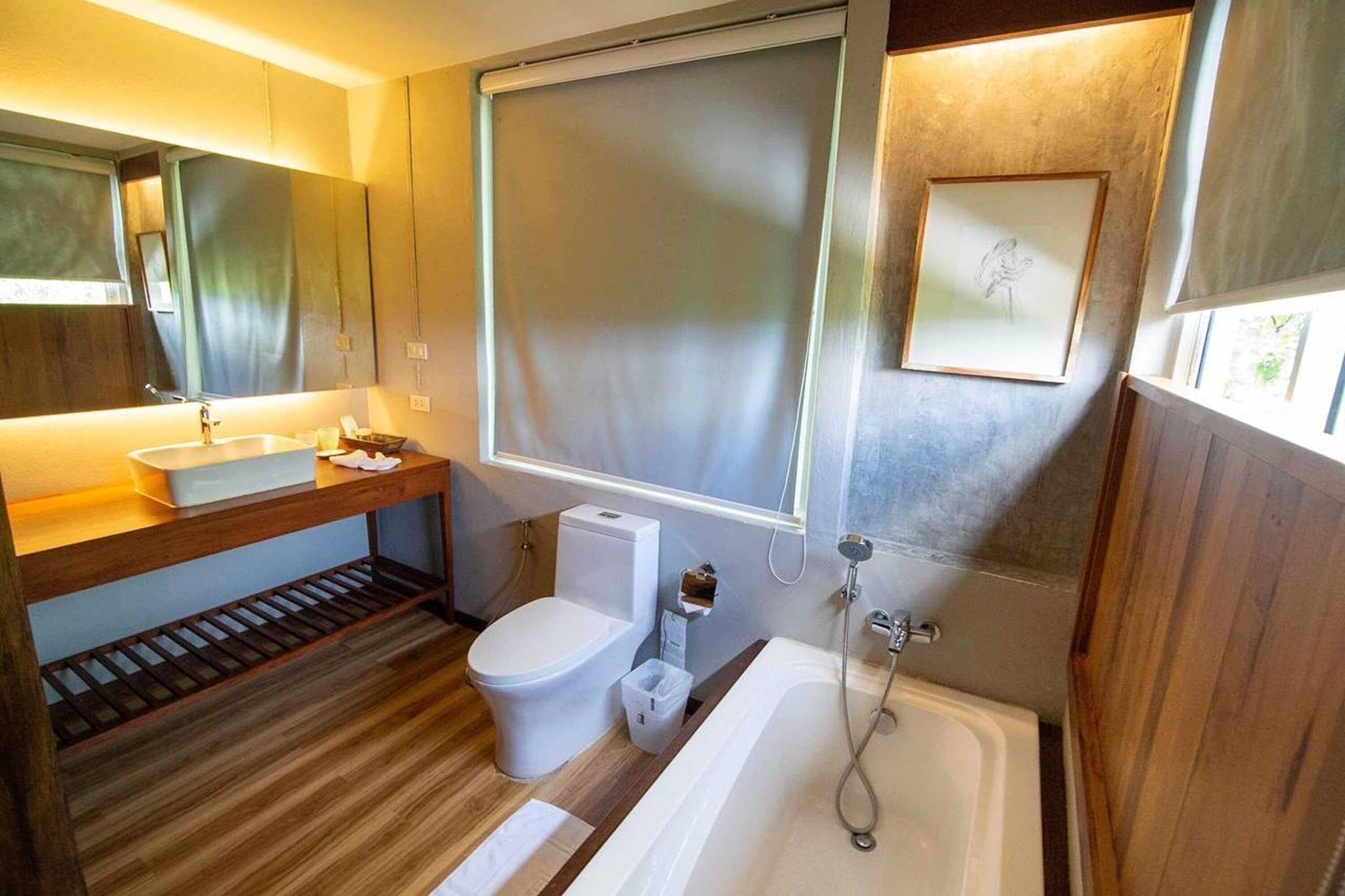 Une salle de bain moderne avec un meuble-lavabo en bois, des toilettes, une baignoire et une grande fenêtre.