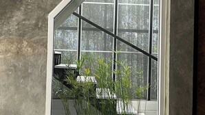 Une pièce avec un mur en béton, un climatiseur blanc, une grande fenêtre donnant sur des arbres et une plante en pot.