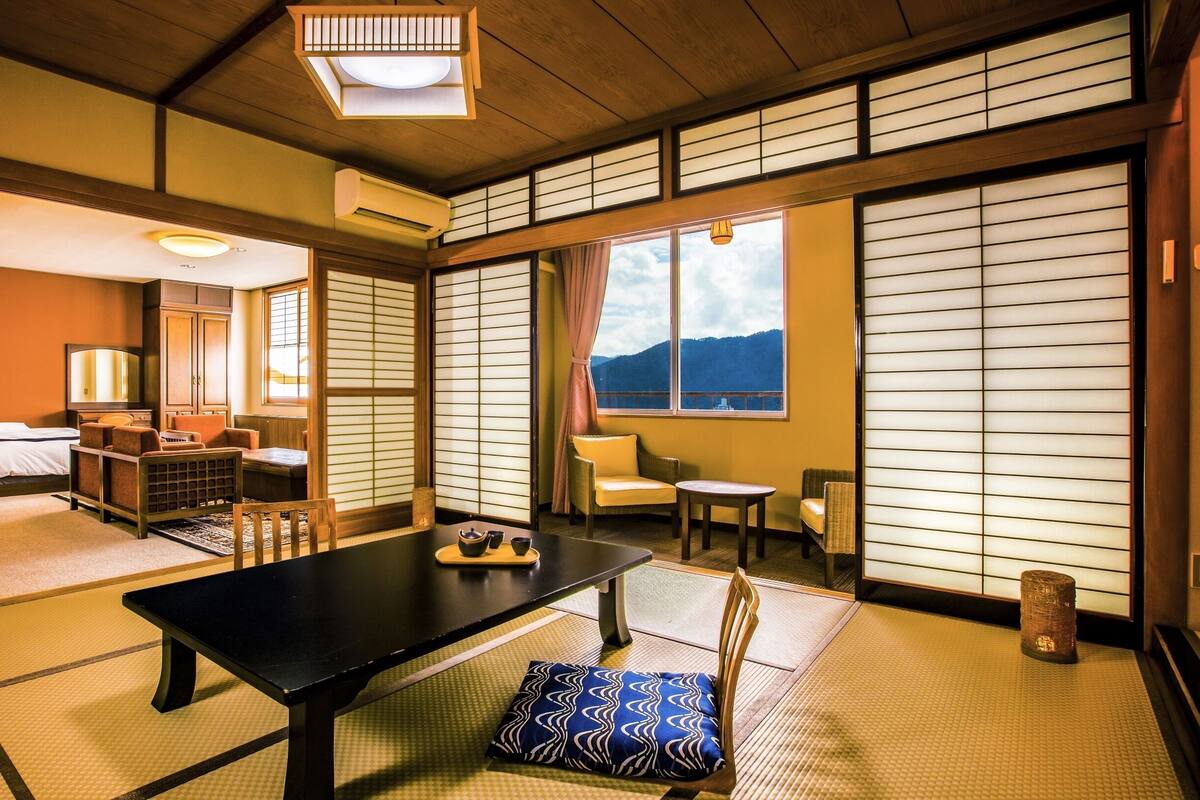 A traditional Japanese-style room with tatami flooring, a low table with a cushion, and sliding shoji doors.