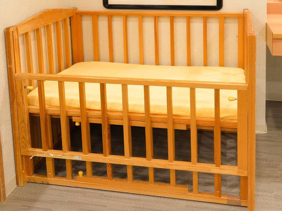 Una cuna de madera con colchón, una mesita de noche de madera y suelo alfombrado.