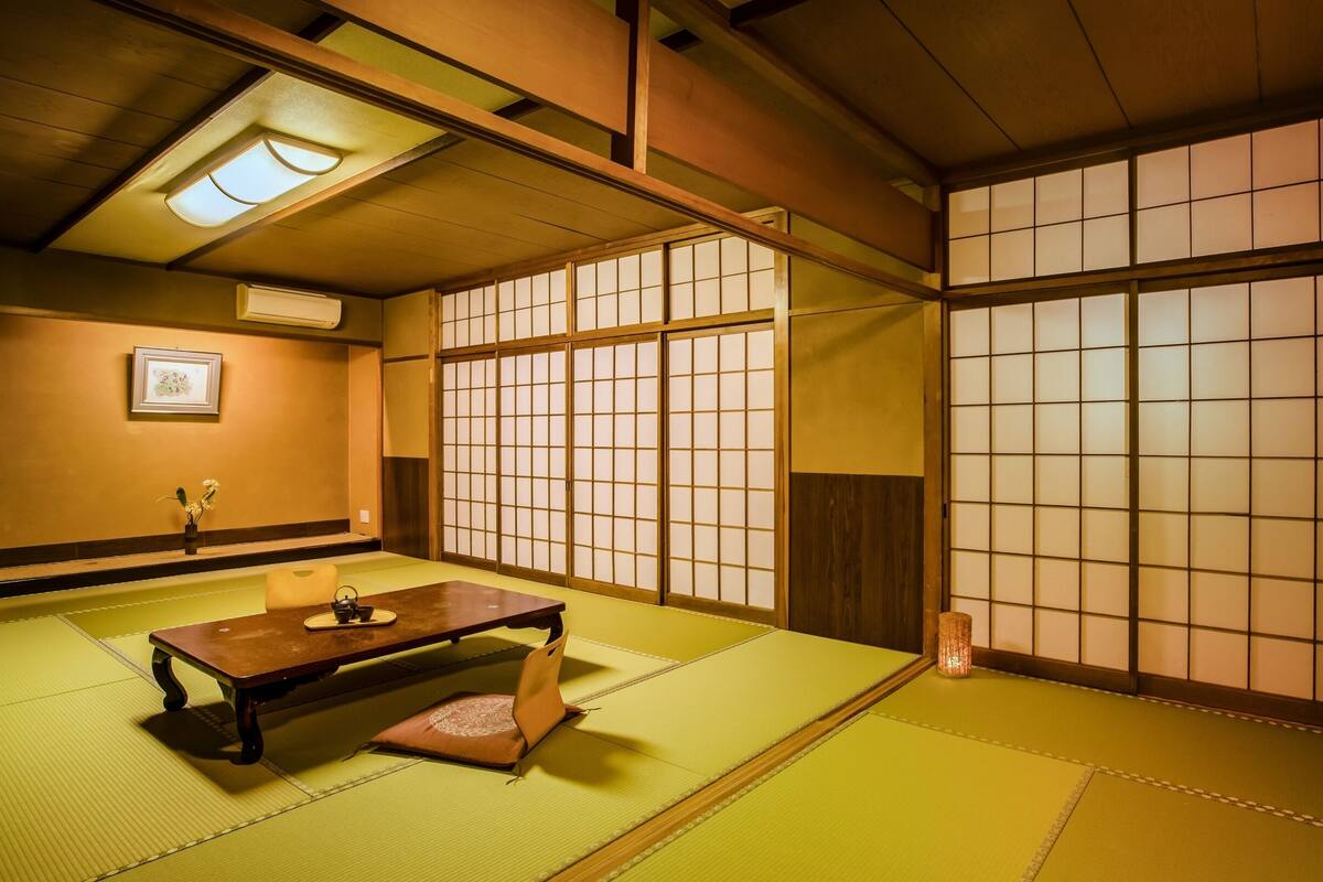 A traditional Japanese room with tatami flooring, a low wooden table, sliding shoji doors, and a ceiling light fixture.