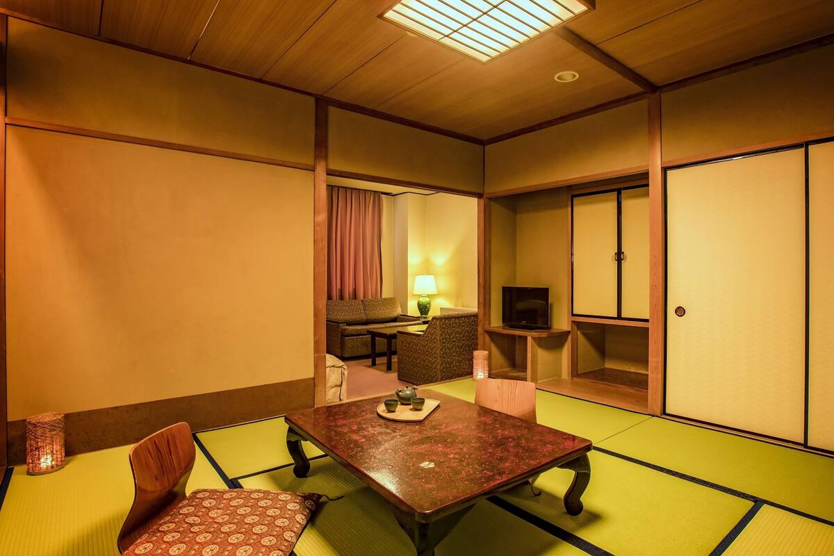 A traditional Japanese room with tatami flooring, a low table with a tea set, a sofa, and a television on a stand.