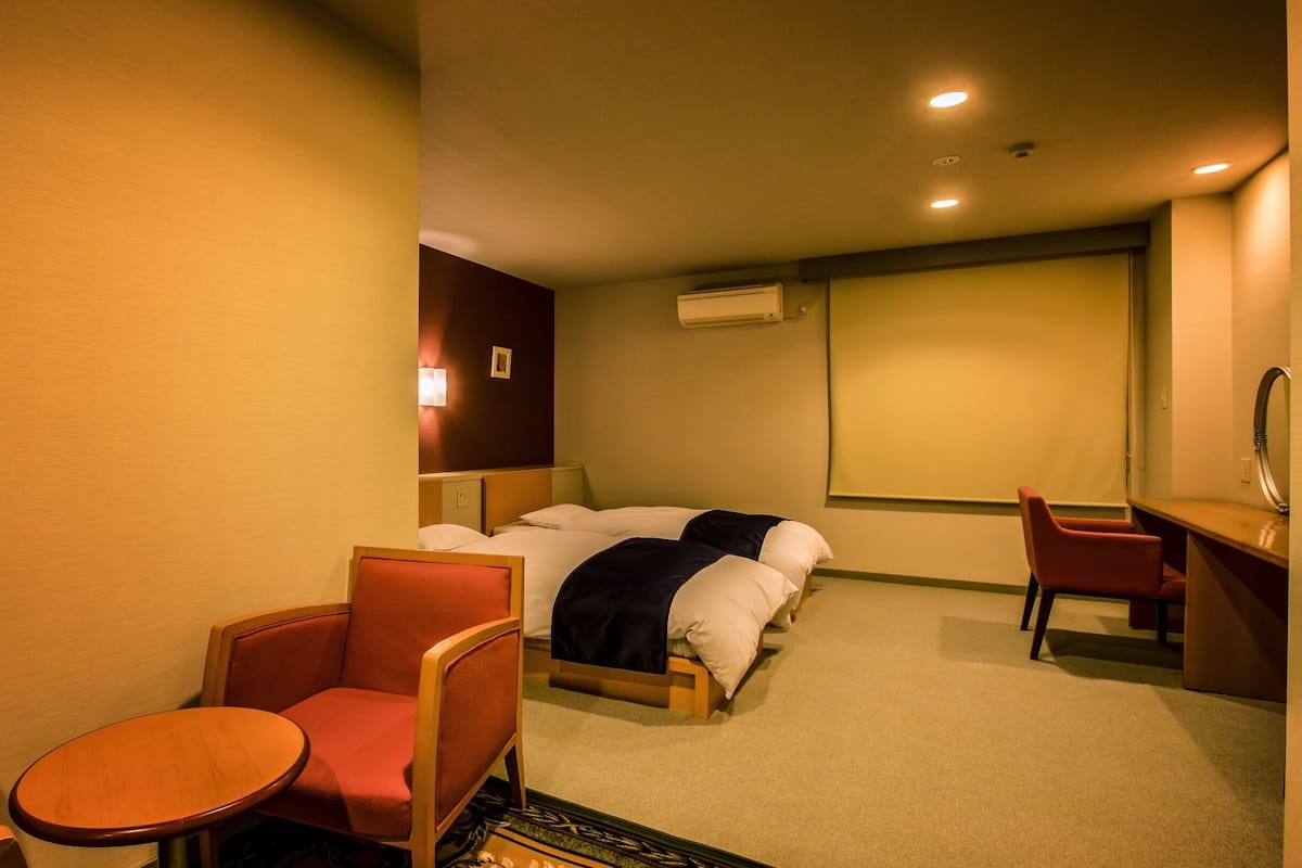 A hotel room with a bed, a desk, a chair, and a small table.