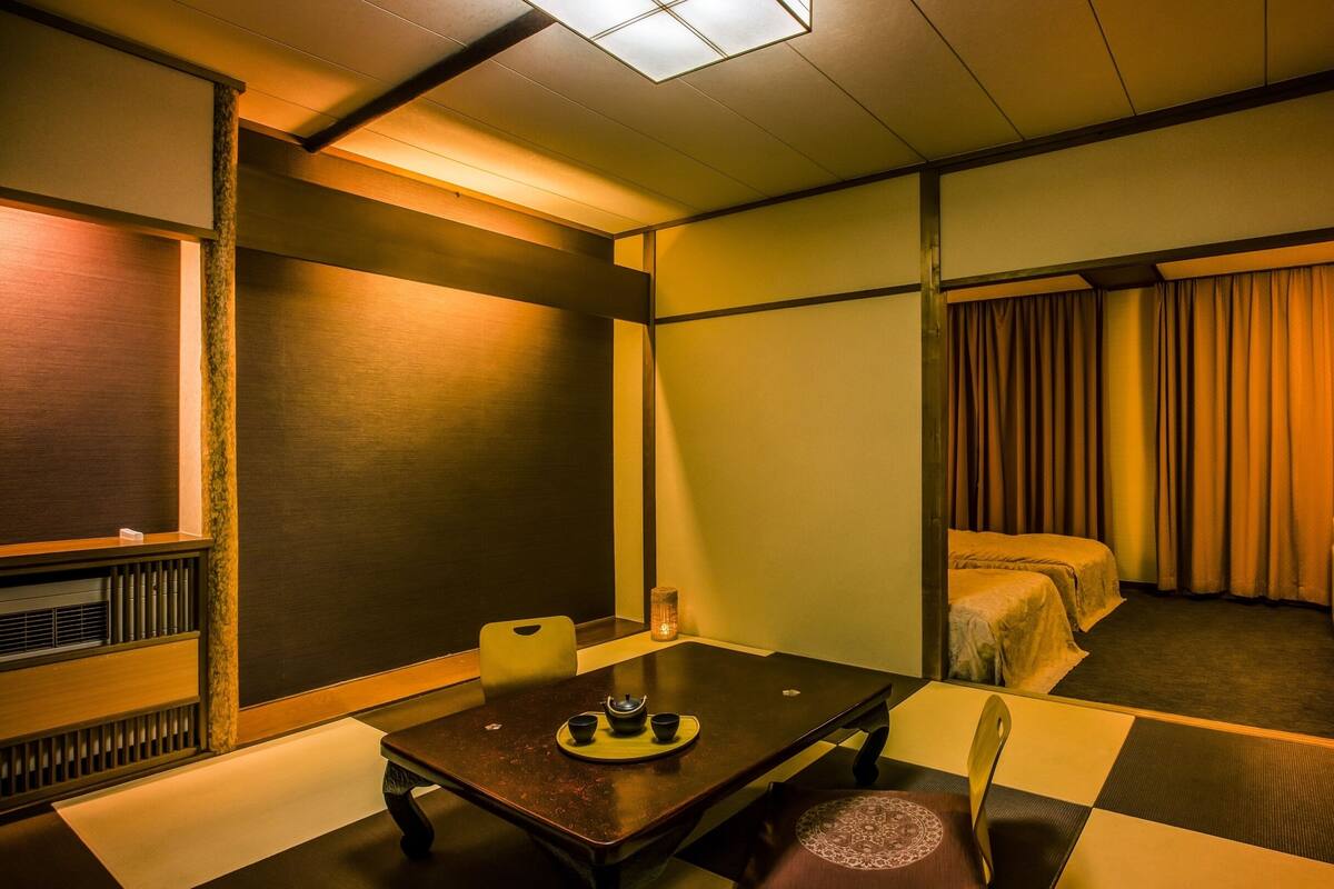 A hotel room with a checkered floor, a wooden table with a tea set, a bed with curtains, and a radiator.