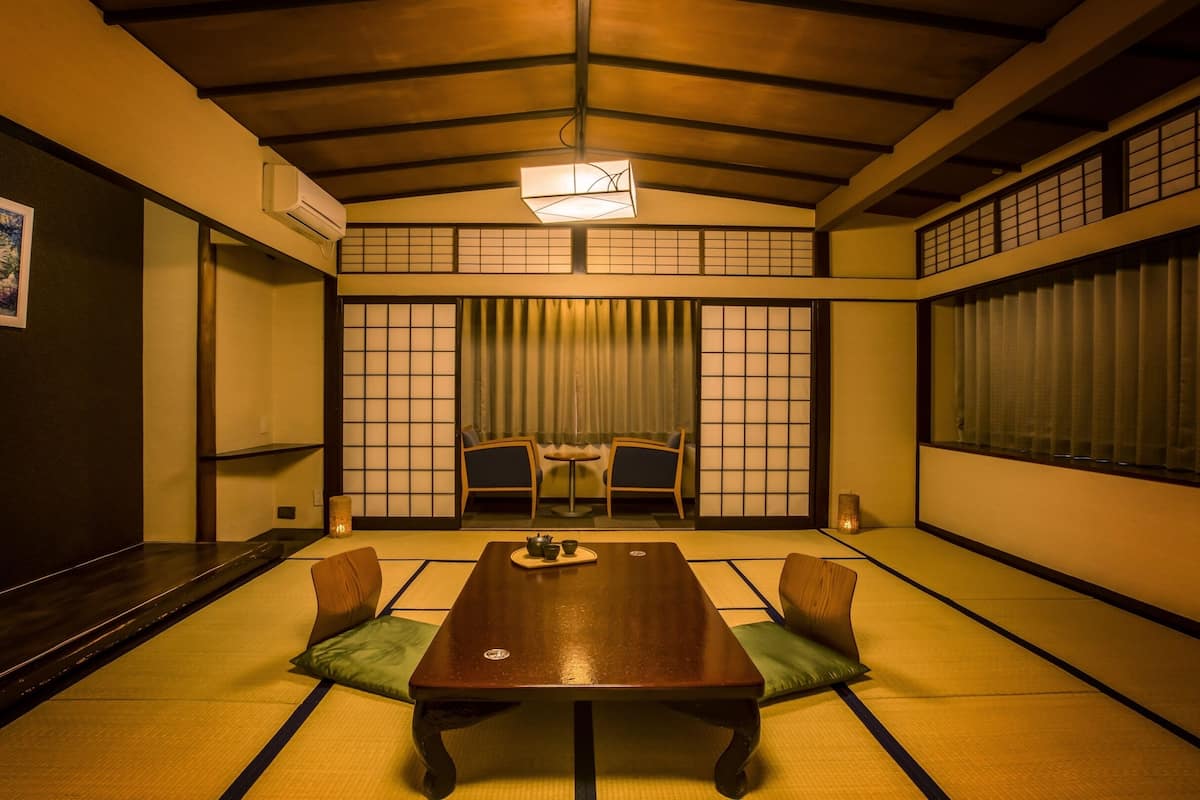 A traditional Japanese room with tatami flooring, a low table, two chairs, a sliding door with shoji screens, and a ceiling fan.