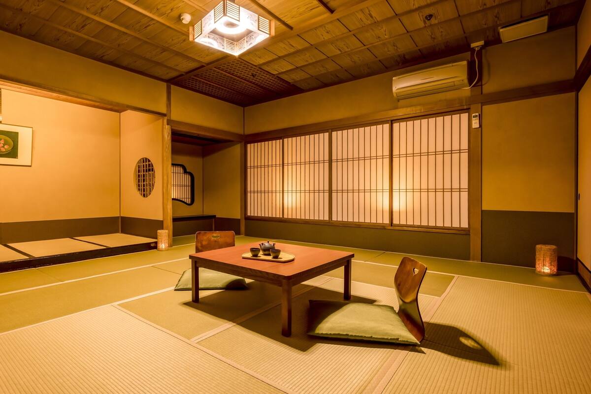 A traditional Japanese room with tatami flooring, a low wooden table with tea set, shoji screens, and a hanging light fixture.