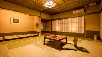 Um quarto japonês tradicional com tatames, uma mesa de madeira baixa com conjunto de chá, biombos shoji e um candeeiro pendente.