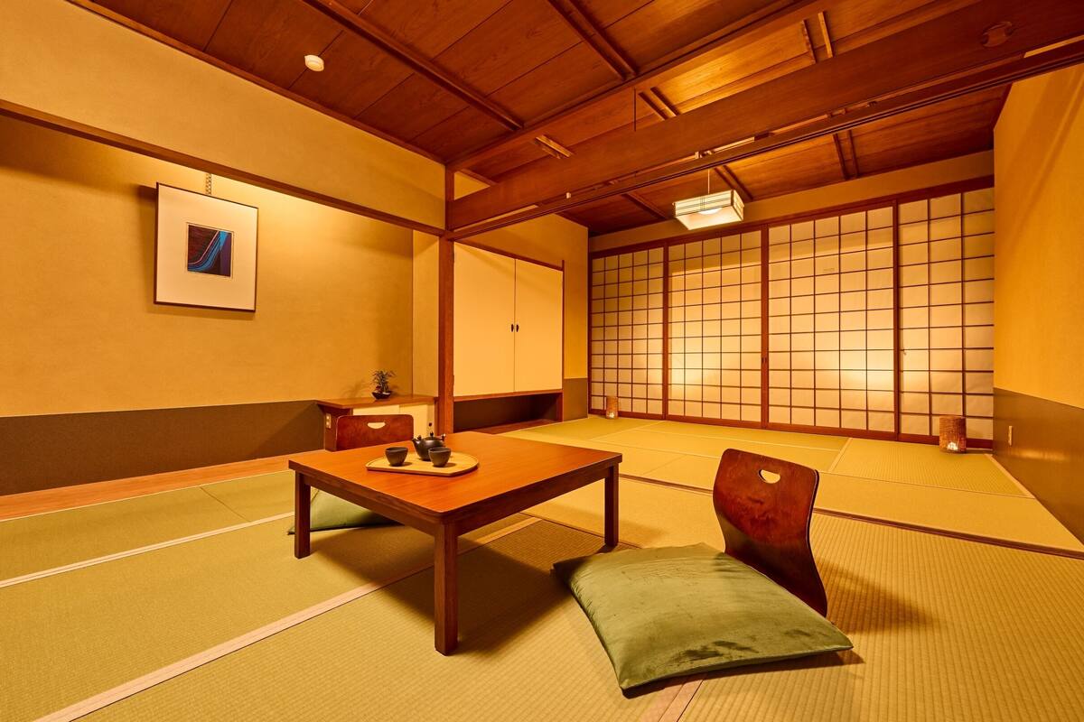 A traditional Japanese room with tatami flooring, a low wooden table, a green cushion, and a shoji screen in the background.