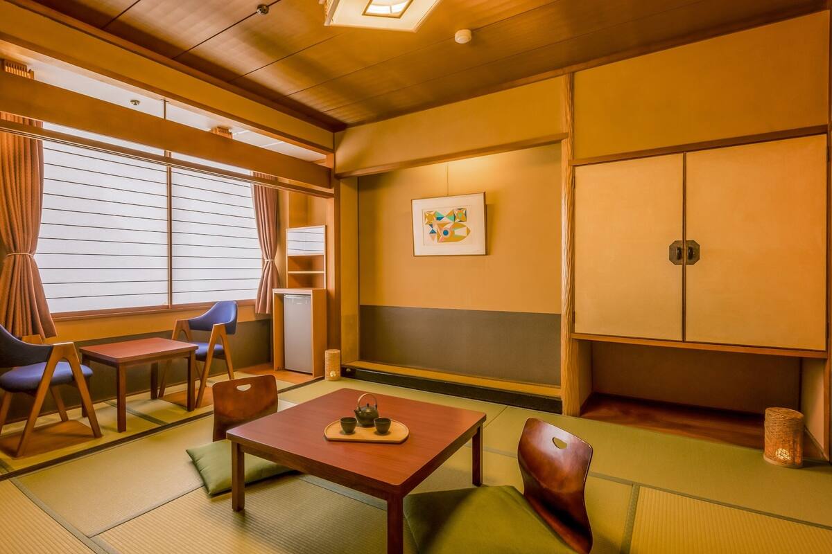 A traditional Japanese room with tatami flooring, a low table with a tea set, and a shoji screen window.