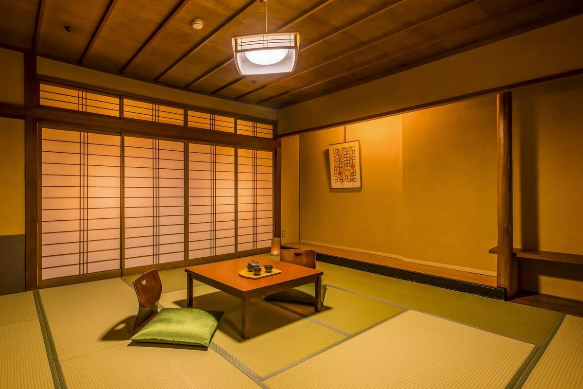 A traditional Japanese room with tatami flooring, a low table with tea set, sliding doors, and a ceiling fan.