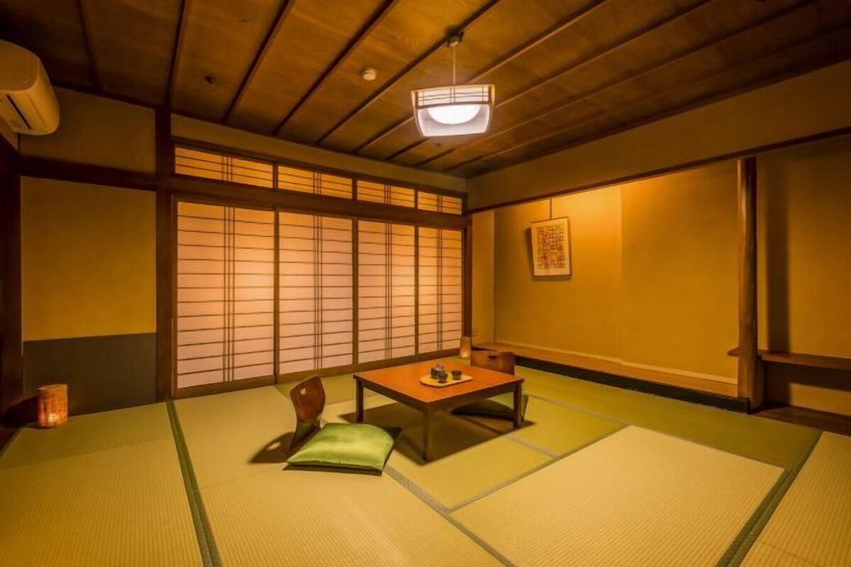 A traditional Japanese room with tatami flooring, a low table, a cushion, and sliding doors.