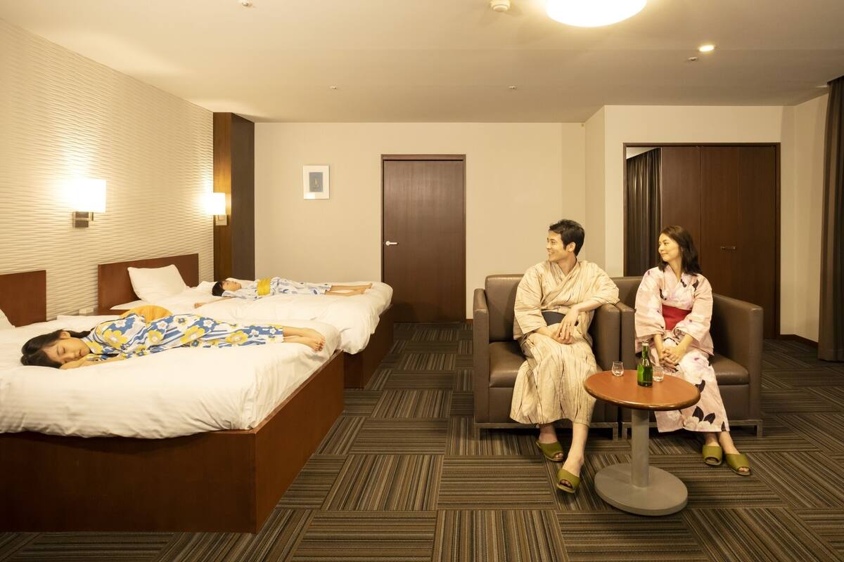 A hotel room with a large bed, two smaller beds, a sofa, and a small table.