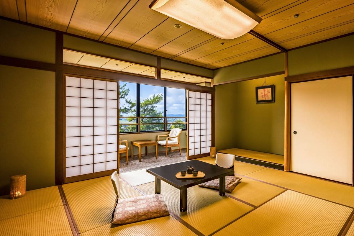 A traditional Japanese room with tatami flooring, a low table with a tea set, and sliding doors leading to a balcony with a view.