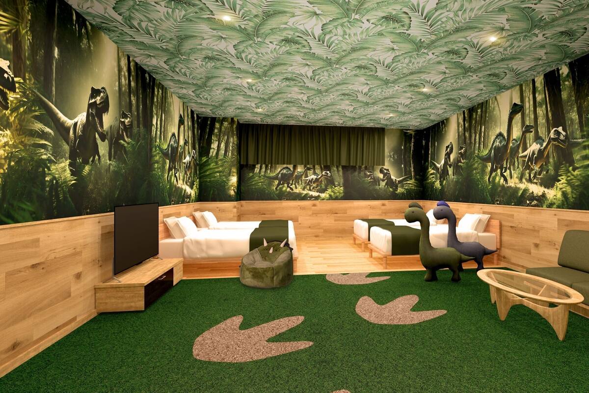 A room with a large mural of dinosaurs, a wooden bed, two sofas, and a small table.