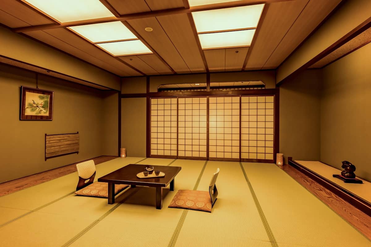 A traditional Japanese room with tatami flooring, a low table with cushions, sliding shoji doors, and a framed picture on the wall.