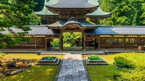 A traditional Japanese building with a tiled roof, wooden pillars, and a stone pathway leading to a pond with plants. - Ooedo Onsen Monogatari Premium Seiunkaku (Awara)