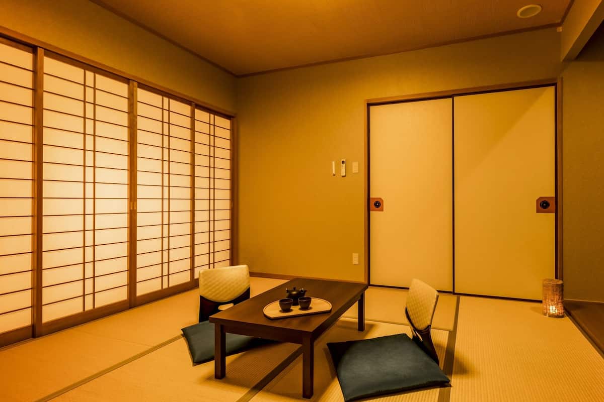 A traditional Japanese room with tatami flooring, a low table with a tea set, and sliding doors.