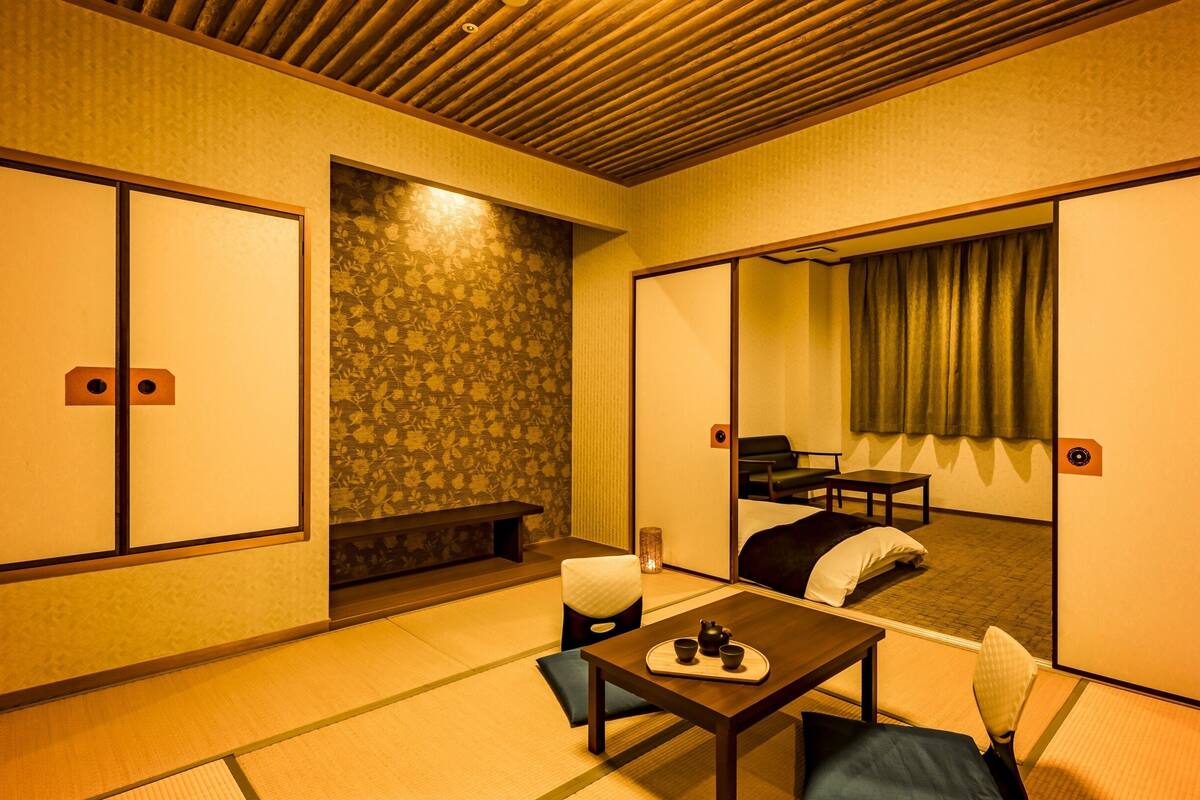 A traditional Japanese room with tatami flooring, a low table with a tea set, a sofa, and a sliding door leading to a balcony.