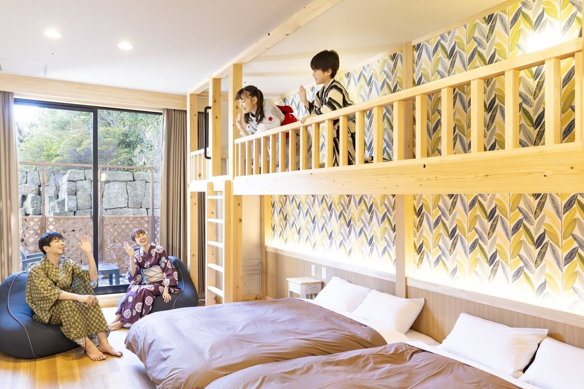 A room with a bunk bed, a desk with a TV, and a large window.