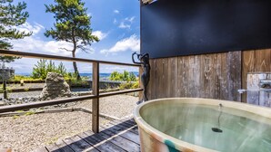 A wooden deck with a hot tub, a stone wall, and a view of the sea. - Ooedo Onsen Monogatari Premium Seiunkaku (Awara)