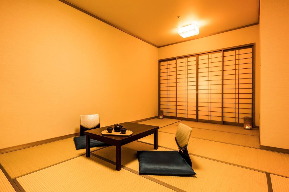 A tatami mat room with a low table, a cushion, a chair, and a sliding door.