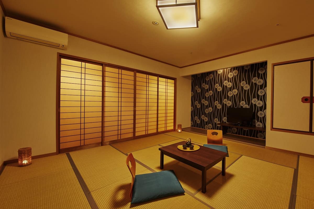 A traditional Japanese room with tatami flooring, a sliding door, a television, and a small table with a tea set.
