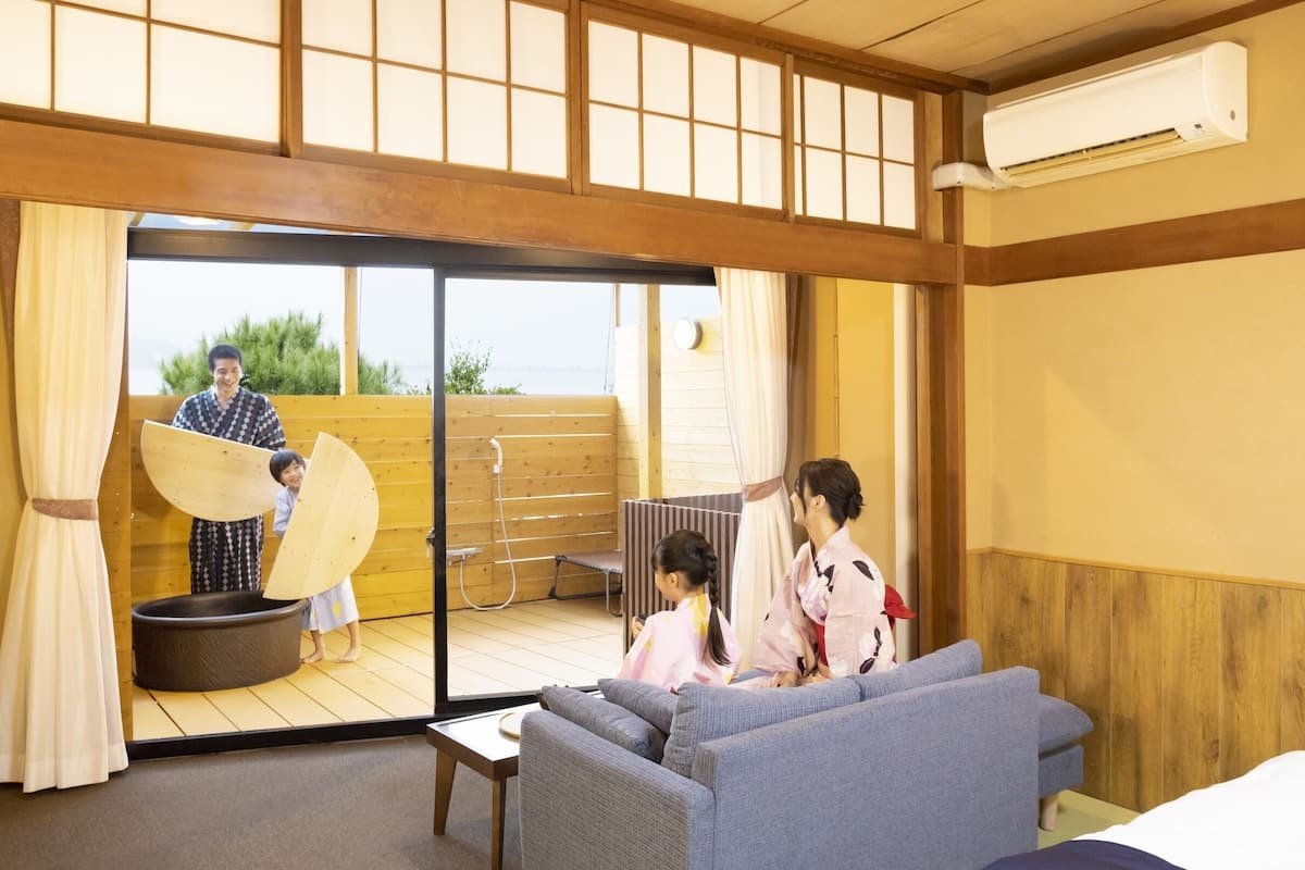 Una habitación japonesa tradicional con suelo de tatami, una puerta corredera de cristal que da a un espacio exterior, un sofá y una cama futón.