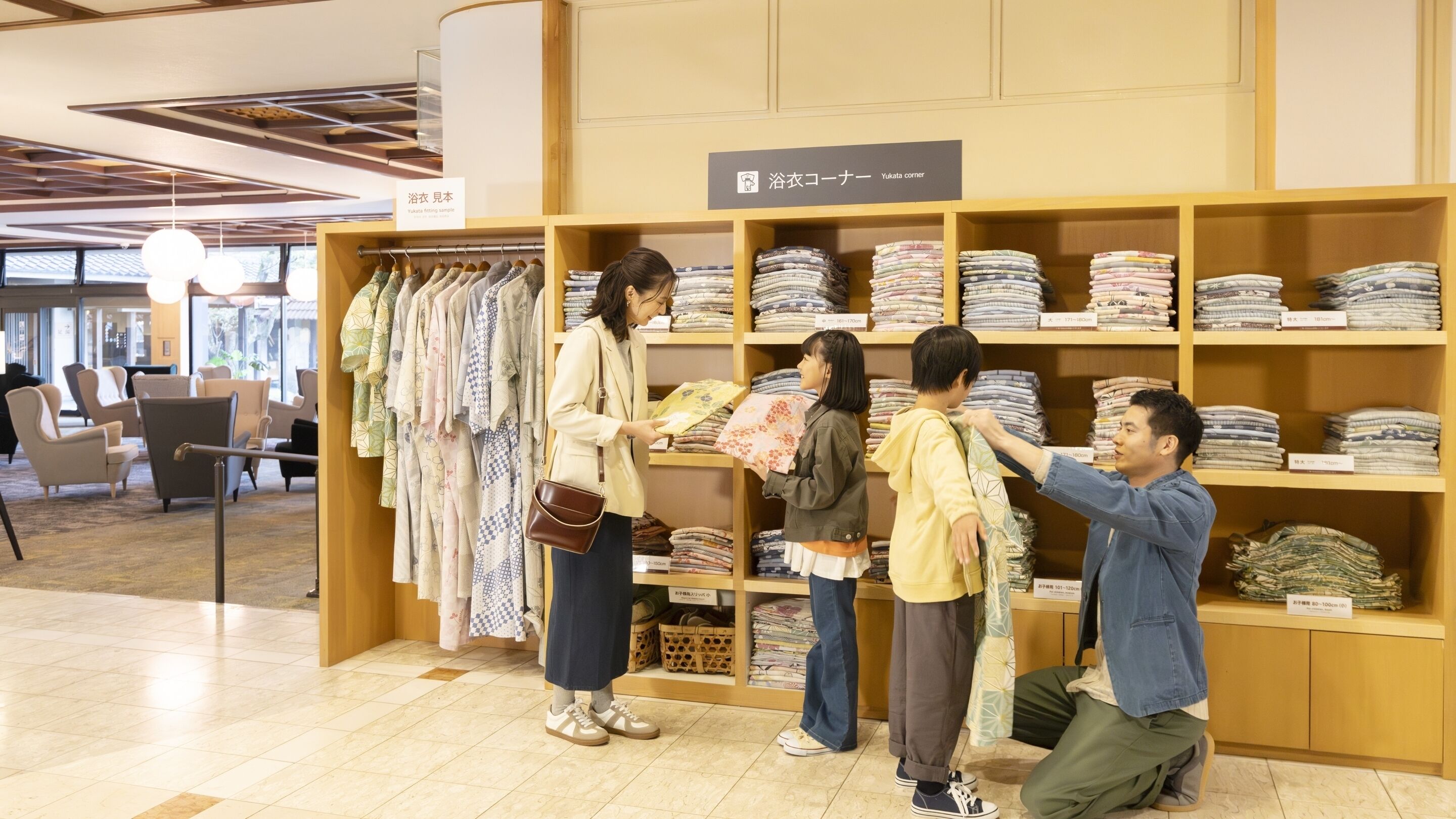 L’intérieur d’un magasin de vêtements, avec des étagères remplies de vêtements pliés, un espace d’essayage et un coin salon avec des chaises.
