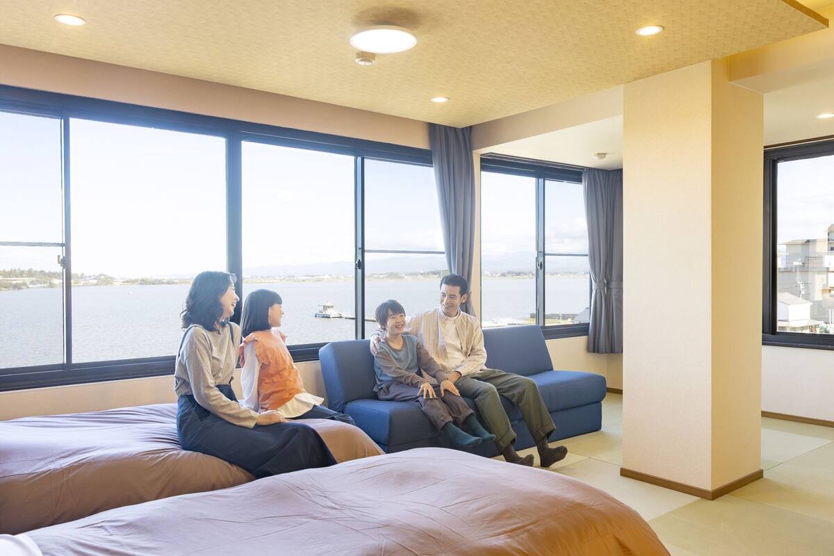 Una habitación con ventanas amplias, un sofá azul y una cama con ropa de cama marrón.