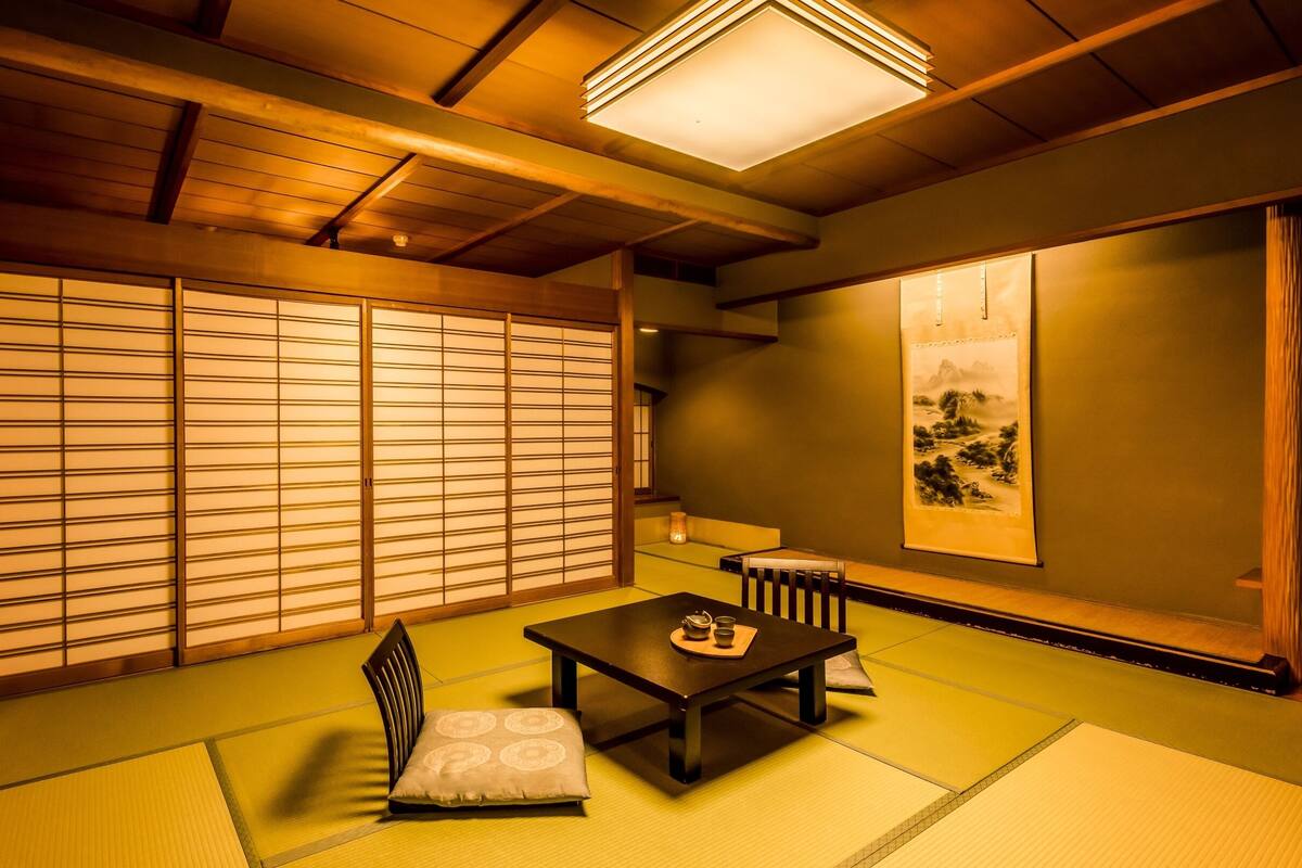 Una habitación japonesa tradicional con suelo de tatami, una mesa baja con cojín, una silla y puertas correderas shoji.